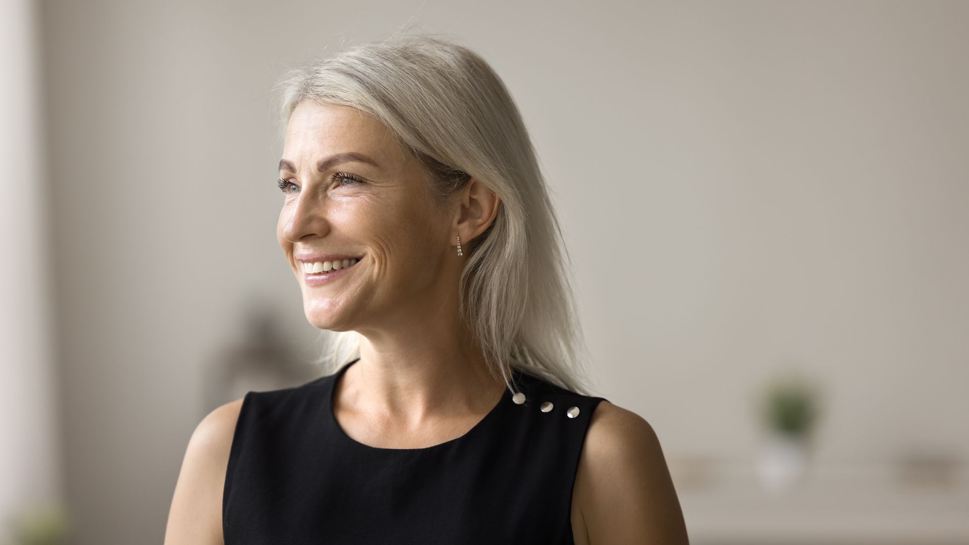 A woman with gray hair is smiling and looking out a window.