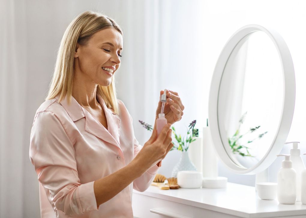 A woman is applying lotion to her face in front of a mirror.