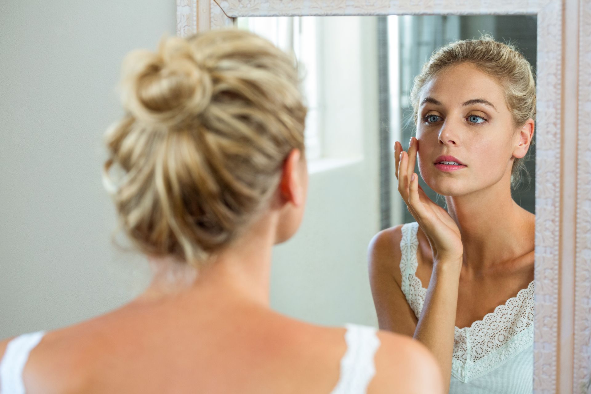 A woman is looking at her face in a mirror.