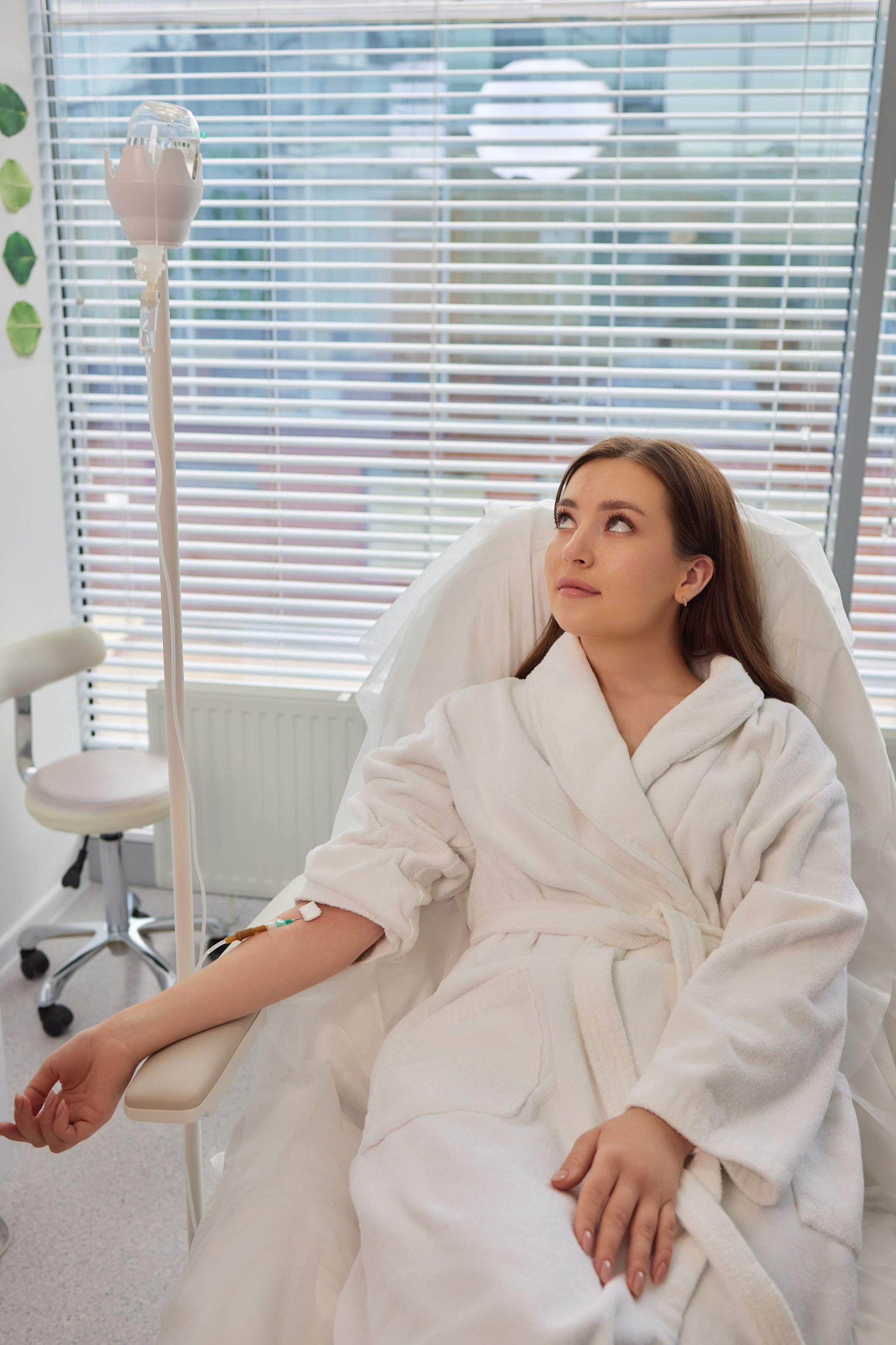 A woman in a bathrobe is sitting in a chair with a drip in her arm.