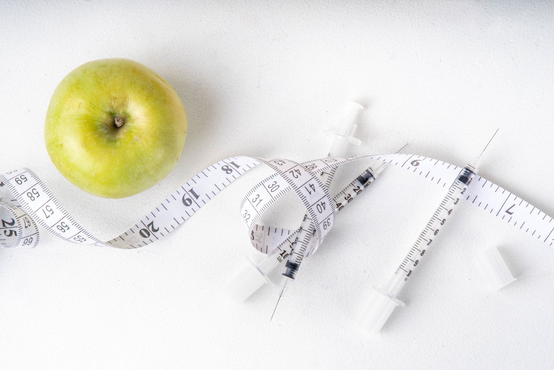 A green apple is sitting next to a measuring tape and a syringe.