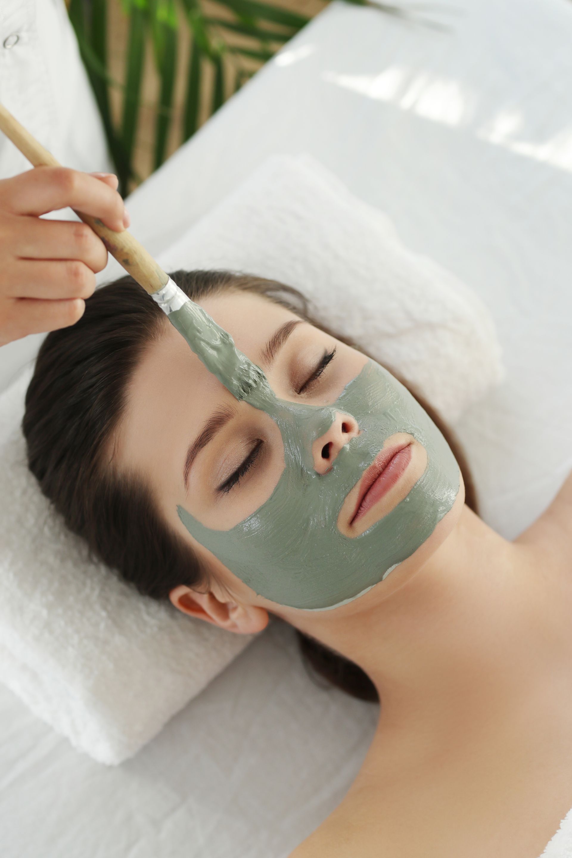 A woman is getting a clay mask on her face at a spa.