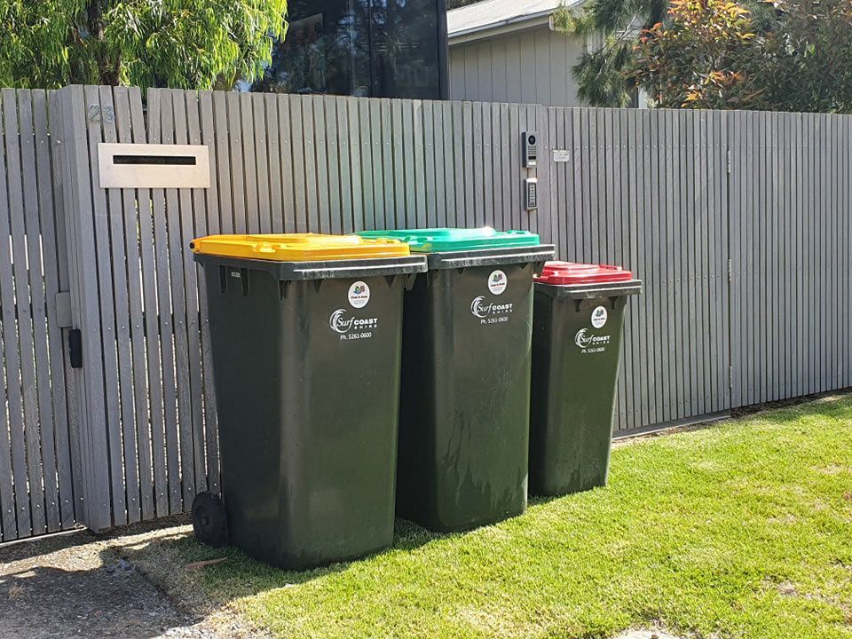 Three Trash Cans Are Lined Up In Front Of A Wooden Fence — Bin in a Bath in Saint Albans Park, VIC