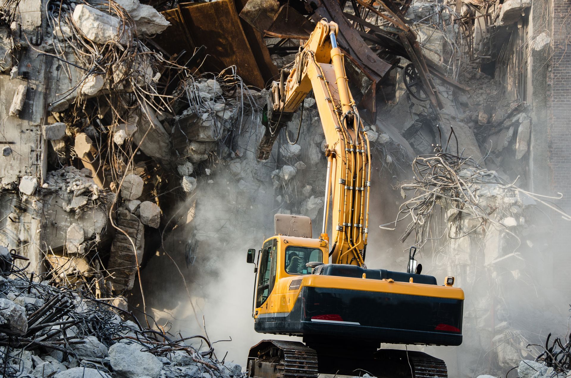 Yellow excavator demolishing a building, creating a cloud of dust.