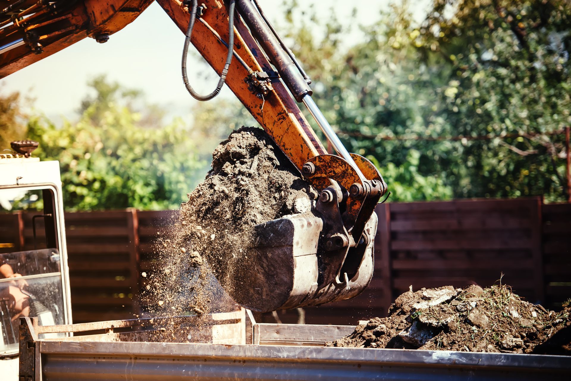 Excavator dumping soil into a truck bed. Orange machine in outdoor construction setting.
