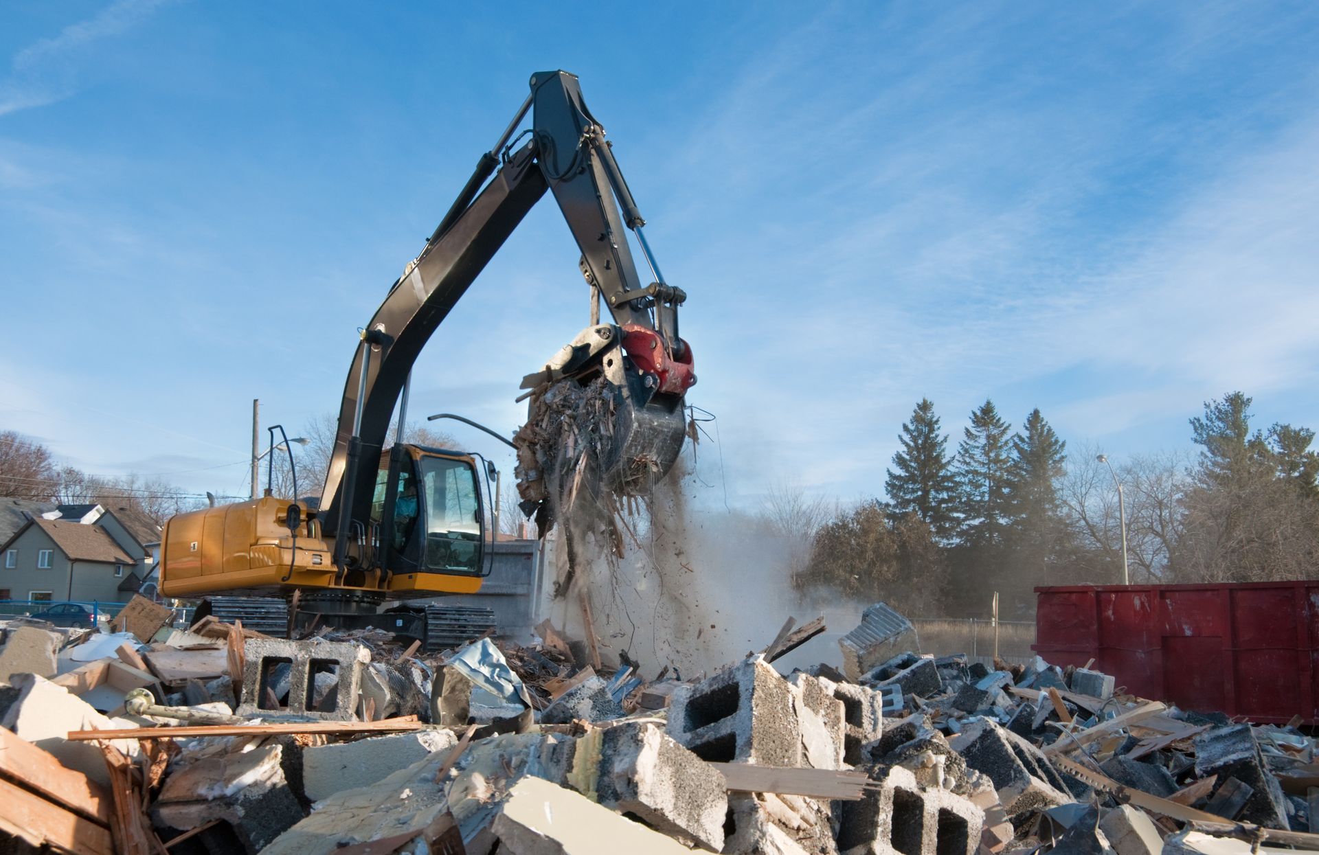 Excavator demolishing a structure, debris falling. Yellow and black machine, blue sky.
