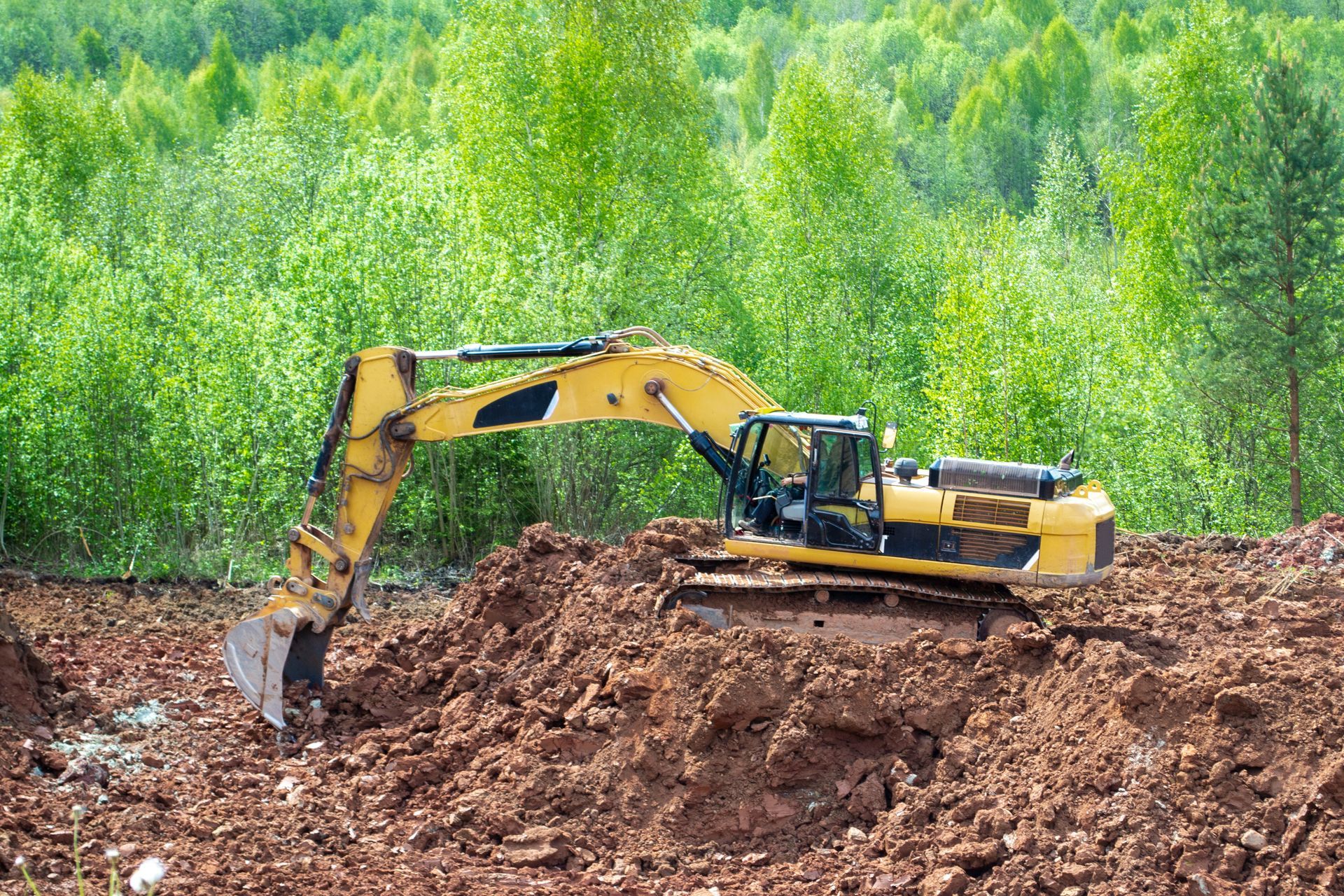 Yellow excavator digging in brown earth, with trees in the background. Yellow excavator digging in brown earth, with trees in the background.