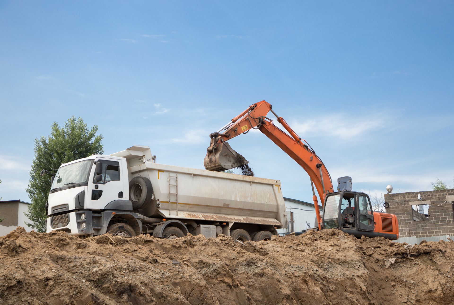An excavator loading dirt into a dump truck on a construction site; blue sky background.