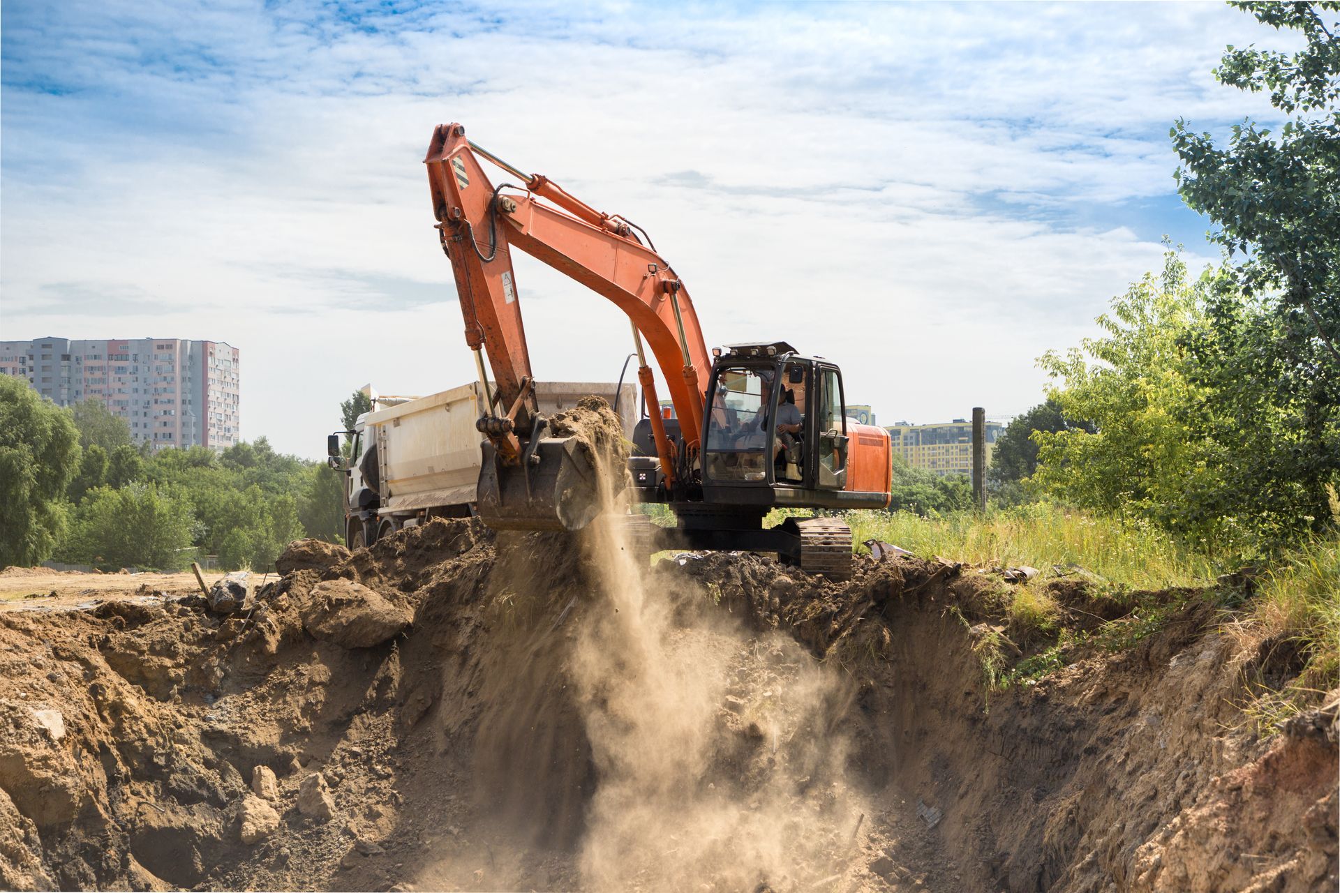 Orange excavator loading dirt into a dump truck at a construction site.