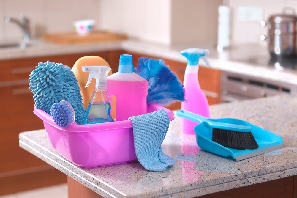 Cleaning supplies in a pink caddy on a kitchen counter, including spray bottles, brushes, and microfiber cloths