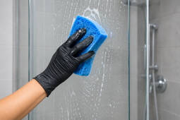 Gloved hands cleaning a white cabinet shelf with a spray bottle and yellow cloth