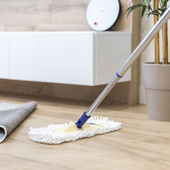 Two cleaners in green overalls and yellow gloves cleaning a bright living room with mop and cloth.