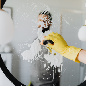 Person in yellow gloves cleaning a mirror with soapy foam