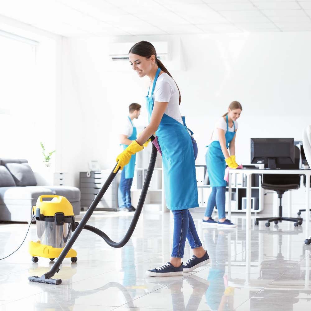 Cleaning staff mopping a bright office floor with a vacuum and desks in the background