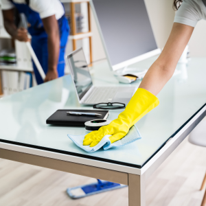 Person in yellow gloves wiping a glass table in a modern office