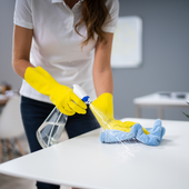 Person in yellow gloves spraying and wiping a white table with a blue cloth