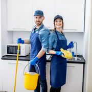 Two cleaners in blue uniforms posing with mop and bucket in a bright kitchen