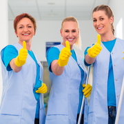 Three smiling lab workers in blue coats and yellow gloves giving thumbs up in a bright laboratory