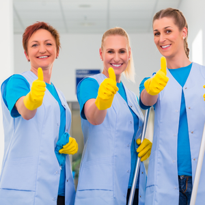 Three smiling lab workers in blue coats and yellow gloves giving thumbs up in a bright laboratory