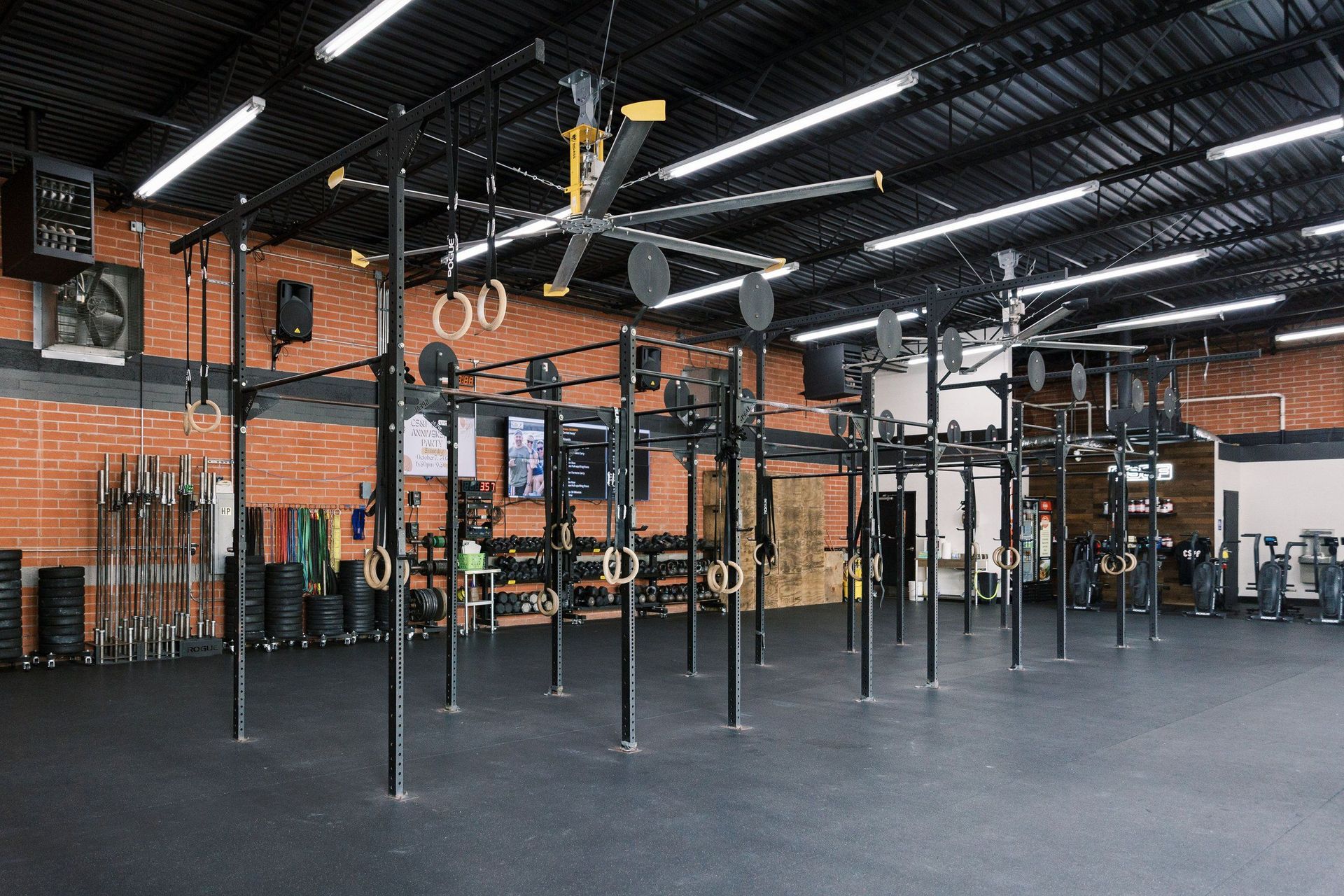 A large empty gym with a lot of equipment and a ceiling fan.