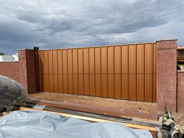 A large brown fence is being built next to a brick wall.