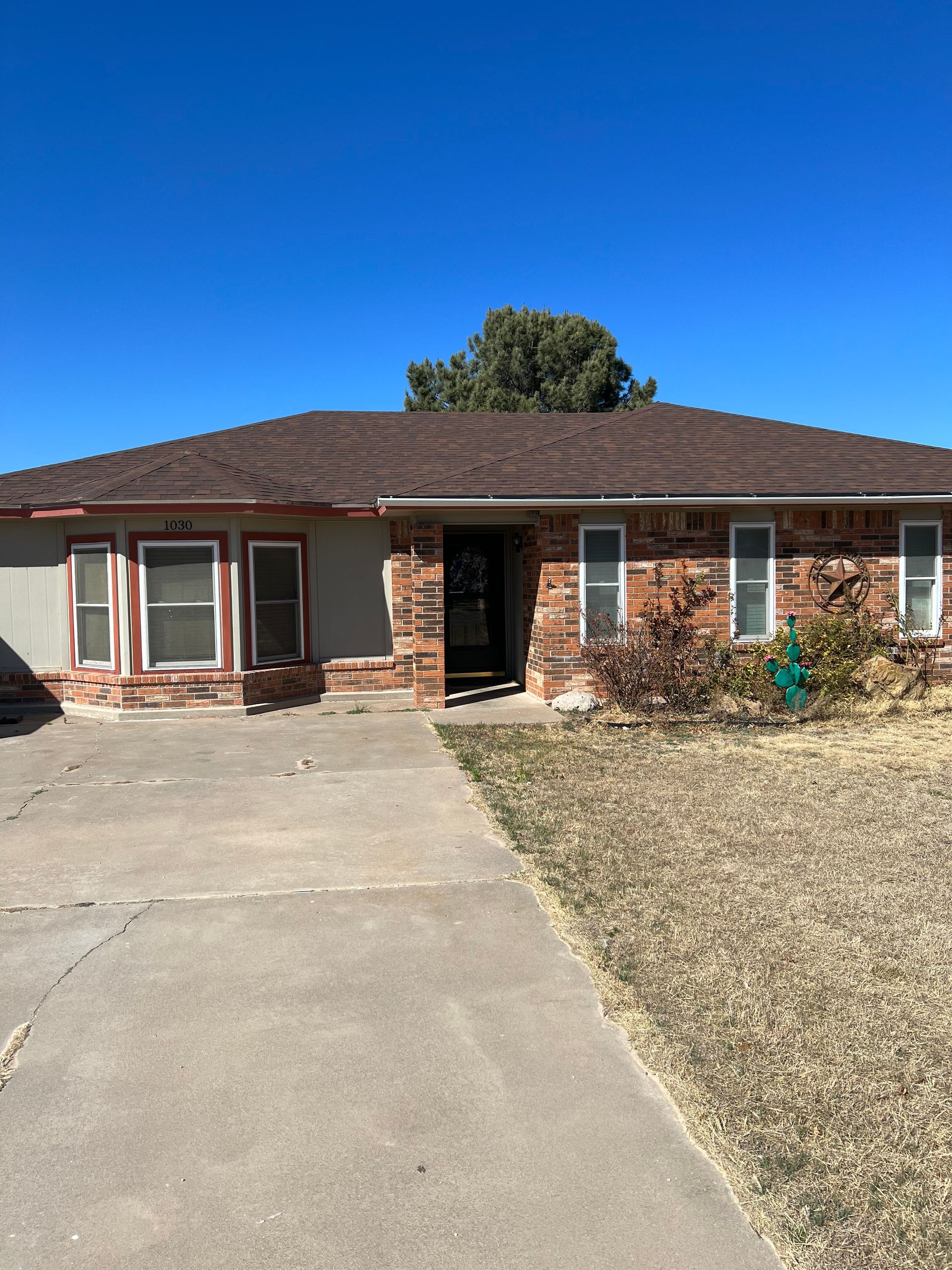 A brick house with a brown roof and a concrete driveway in front of it.