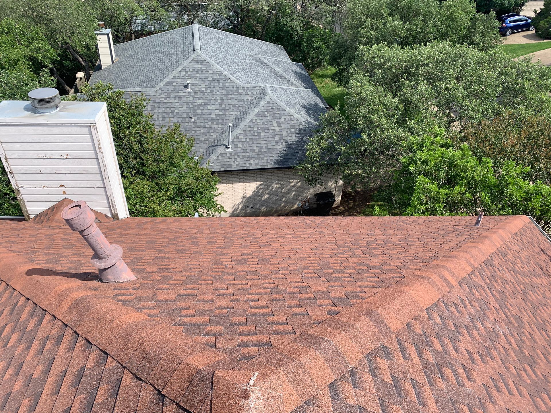A roof with a chimney on it and a house in the background.