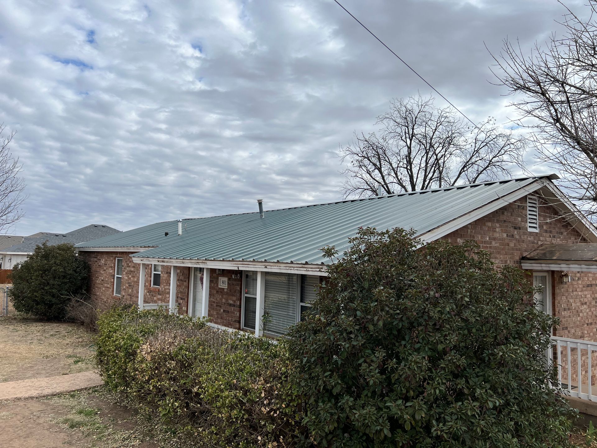 A brick house with a green roof and bushes in front of it.