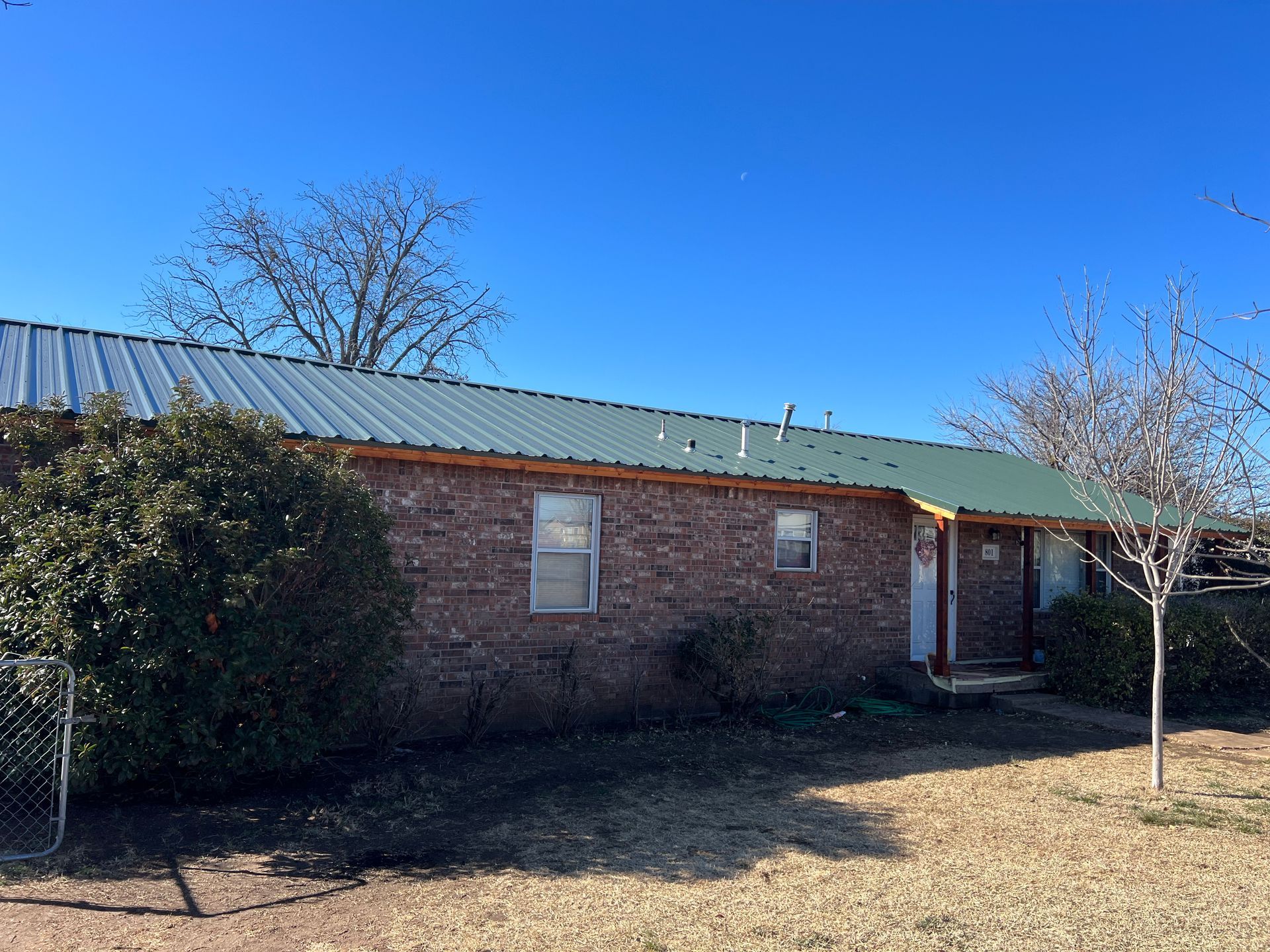 A brick house with a green metal roof and a tree in front of it.
