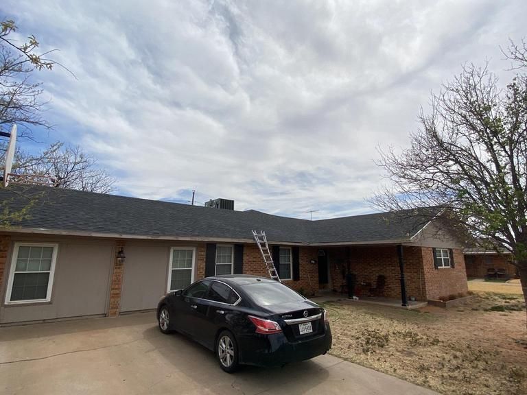 A black car is parked in front of a brick house.