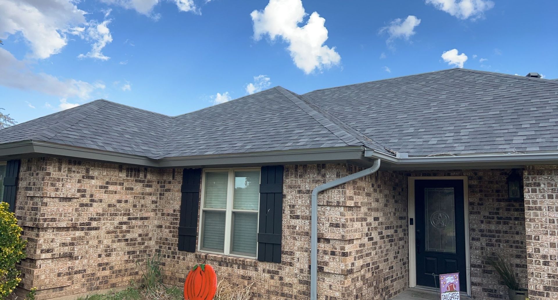 A brick house with a gray roof and black shutters.