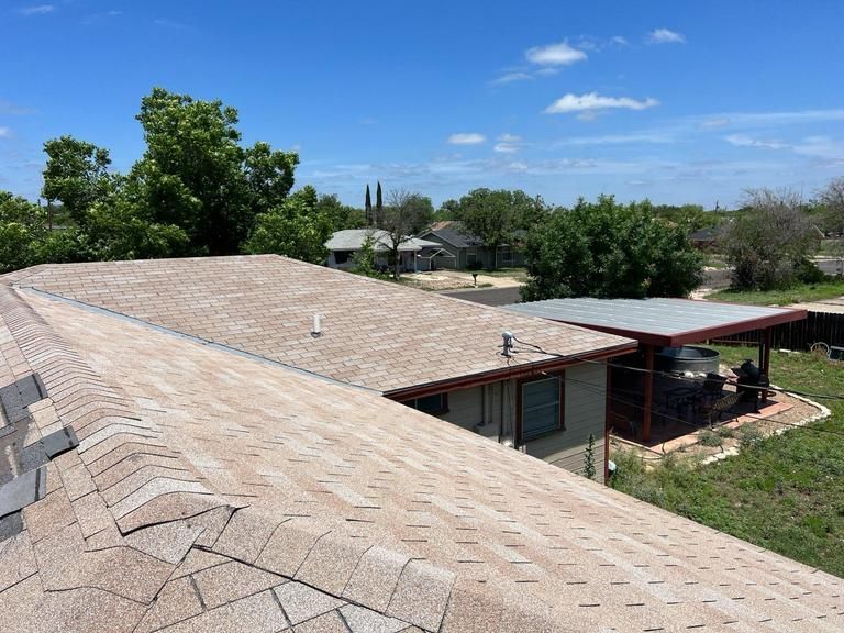 The roof of a house with a carport and trees in the background.