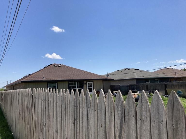 A wooden fence surrounds a house with a blue sky in the background.