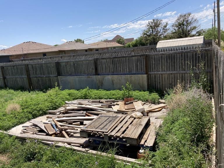 A pile of wood is sitting in the grass next to a fence.