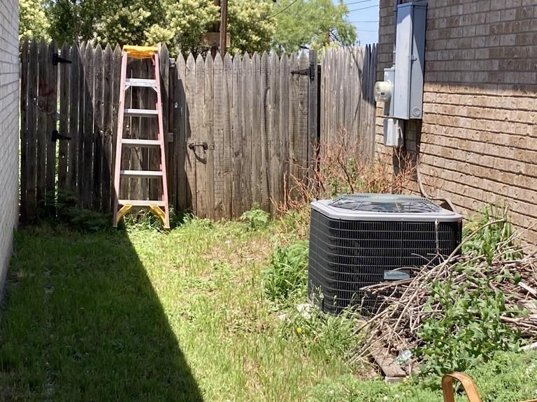 A ladder is sitting in the backyard of a house next to a wooden fence.