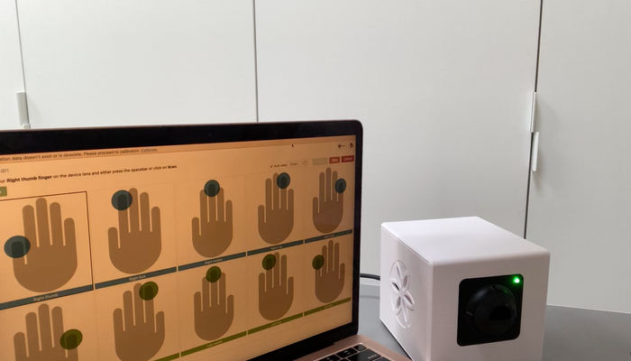 A person presses a finger against a white Bio-Well device. The device has a floral design on the front.