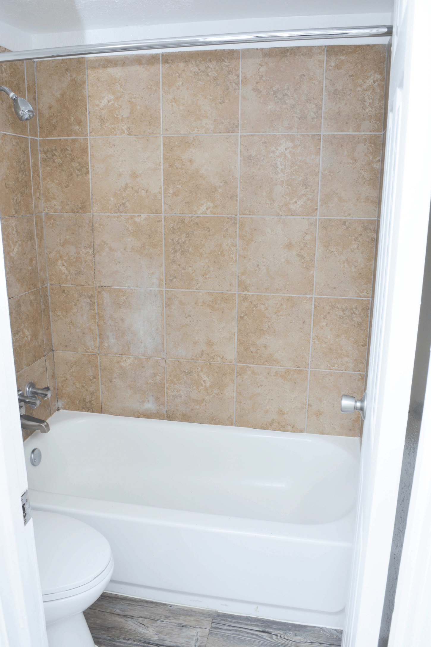 Bathroom with beige tiled shower walls, white tub, and toilet.