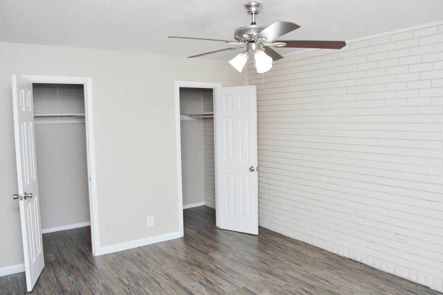 Bedroom with gray wood-look flooring, white brick accent wall, two closets, and a ceiling fan.