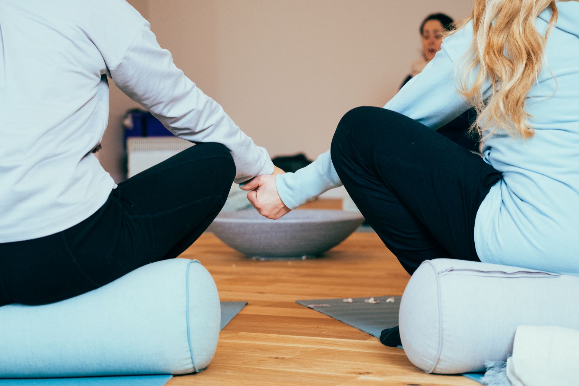 Two people holding hands during a yoga session on bolsters.