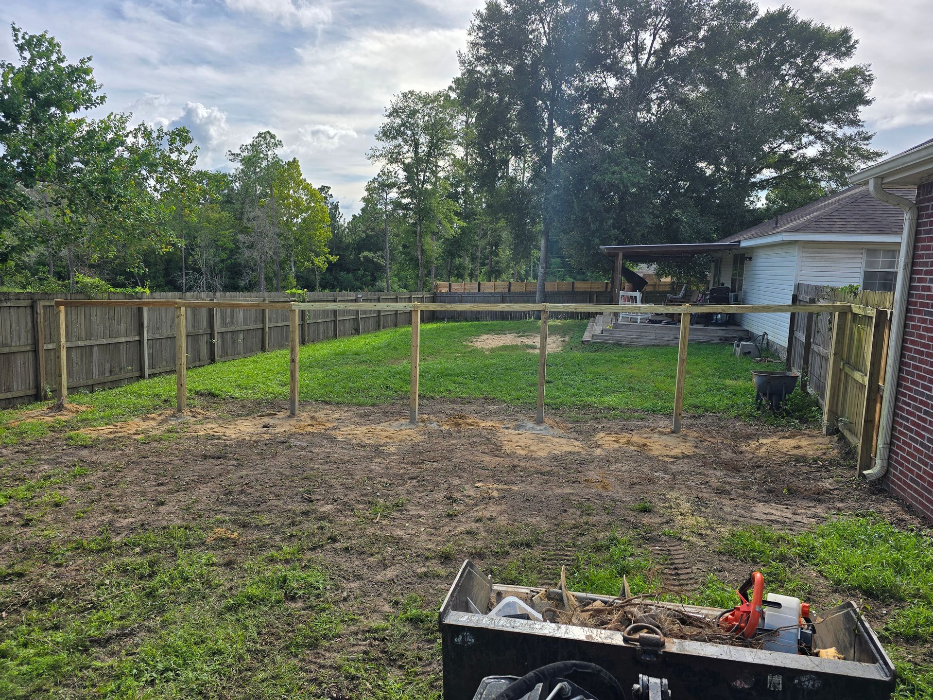 White picket fence along a gravel area and driveway, cars parked nearby a house.