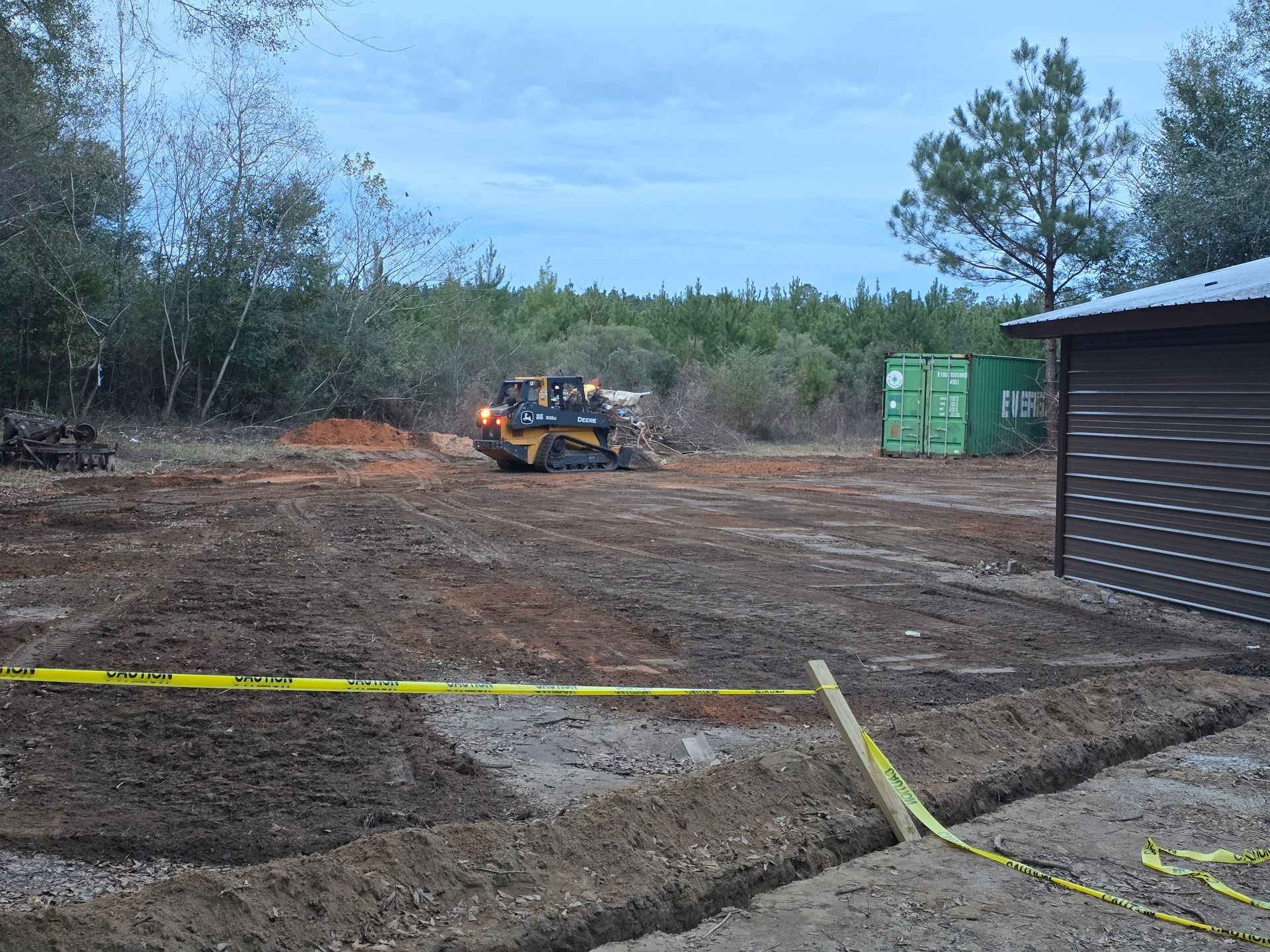 View from a tractor bucket towards a green field, tree, and treeline under a blue sky.