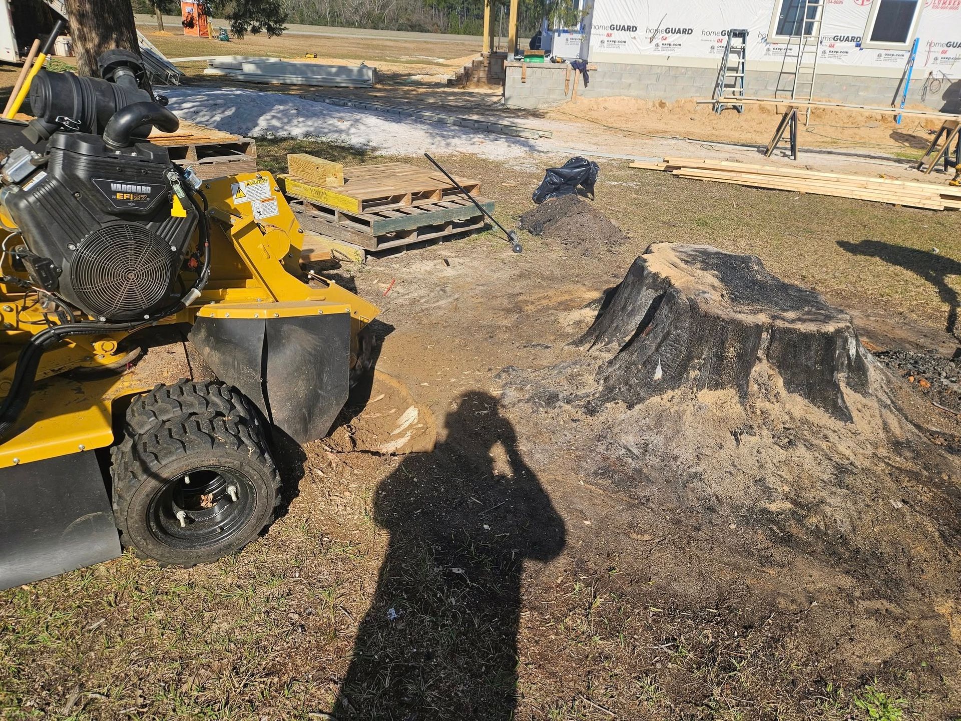 A yellow stump grinder next to a freshly ground tree stump on a construction site.