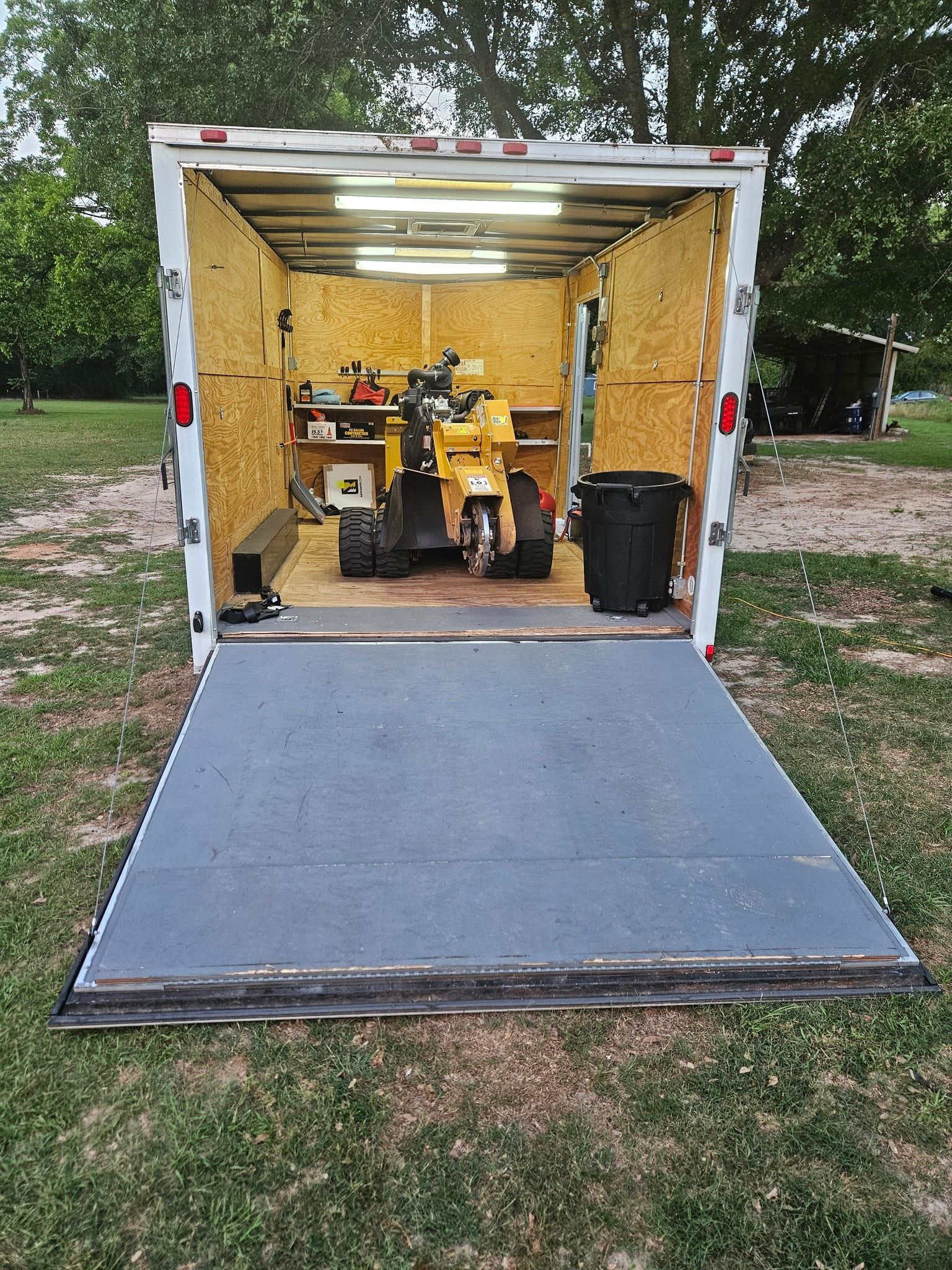 Open cargo trailer with ramp down. Inside, a machine, workbench, and trash can are visible.