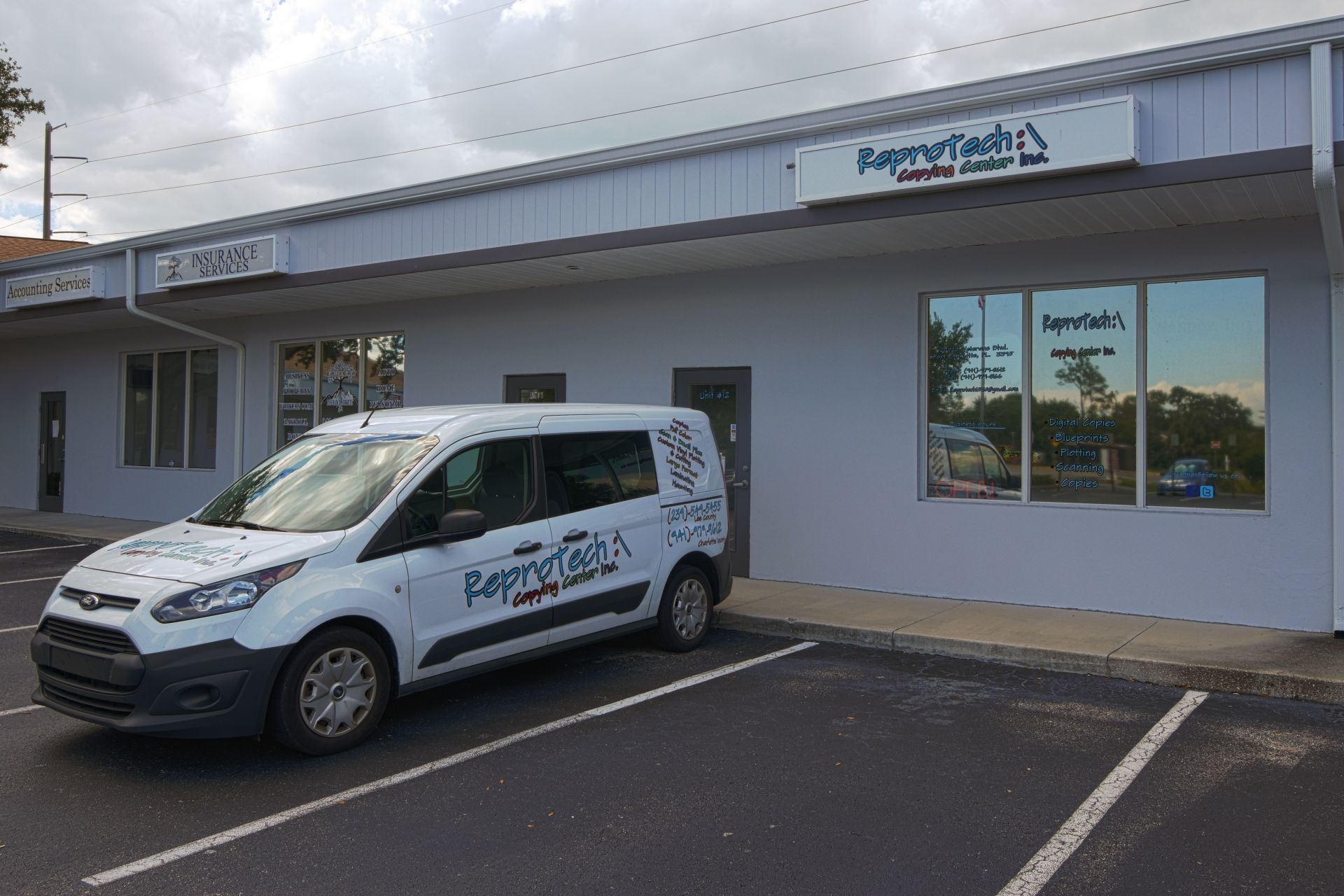 White van parked in front of a business named RepairTech, next to other businesses in a strip mall.