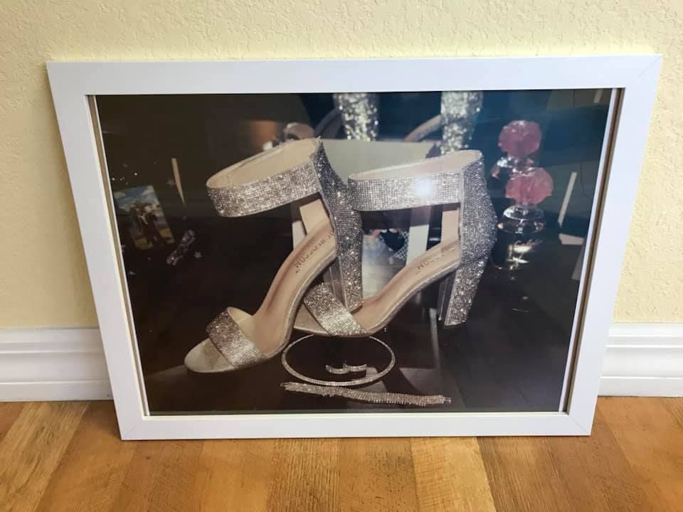 Framed photograph of sparkly high-heeled sandals, displayed on a reflective surface.