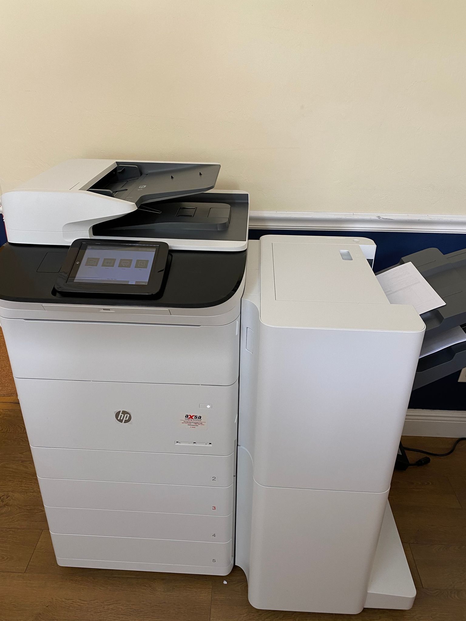 White HP multi-function printer, with touchscreen and paper output, against a beige wall.