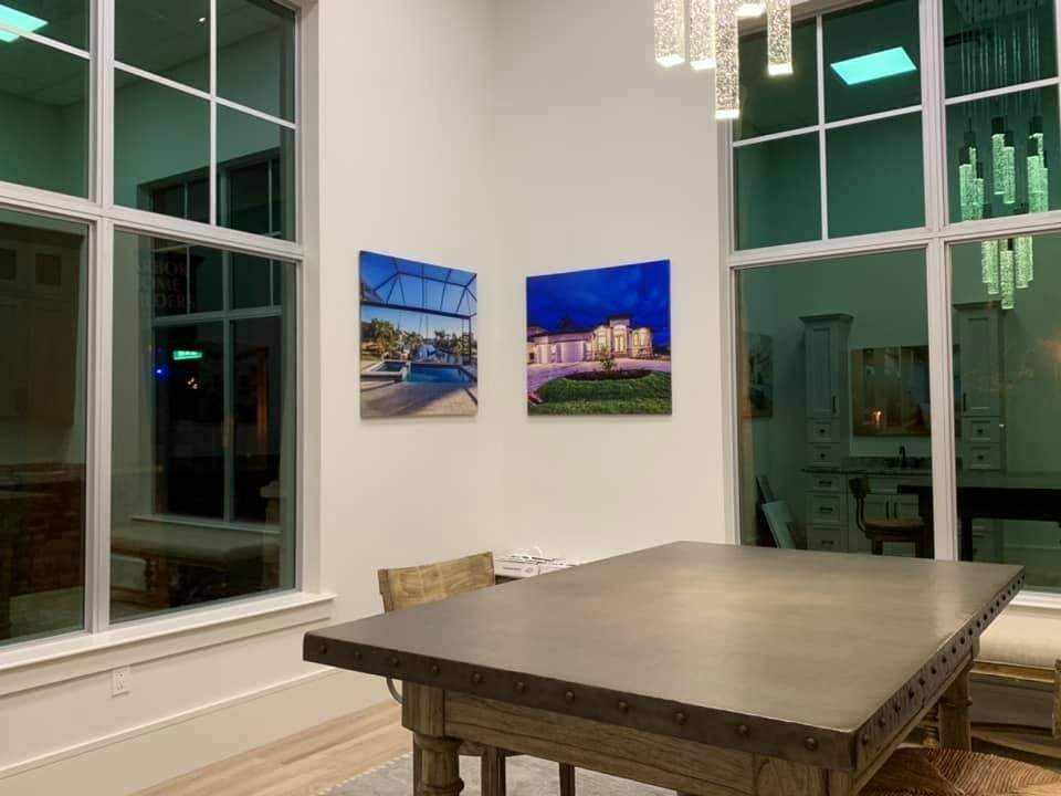 Two paintings on white wall in room with large windows, table, and chandelier.
