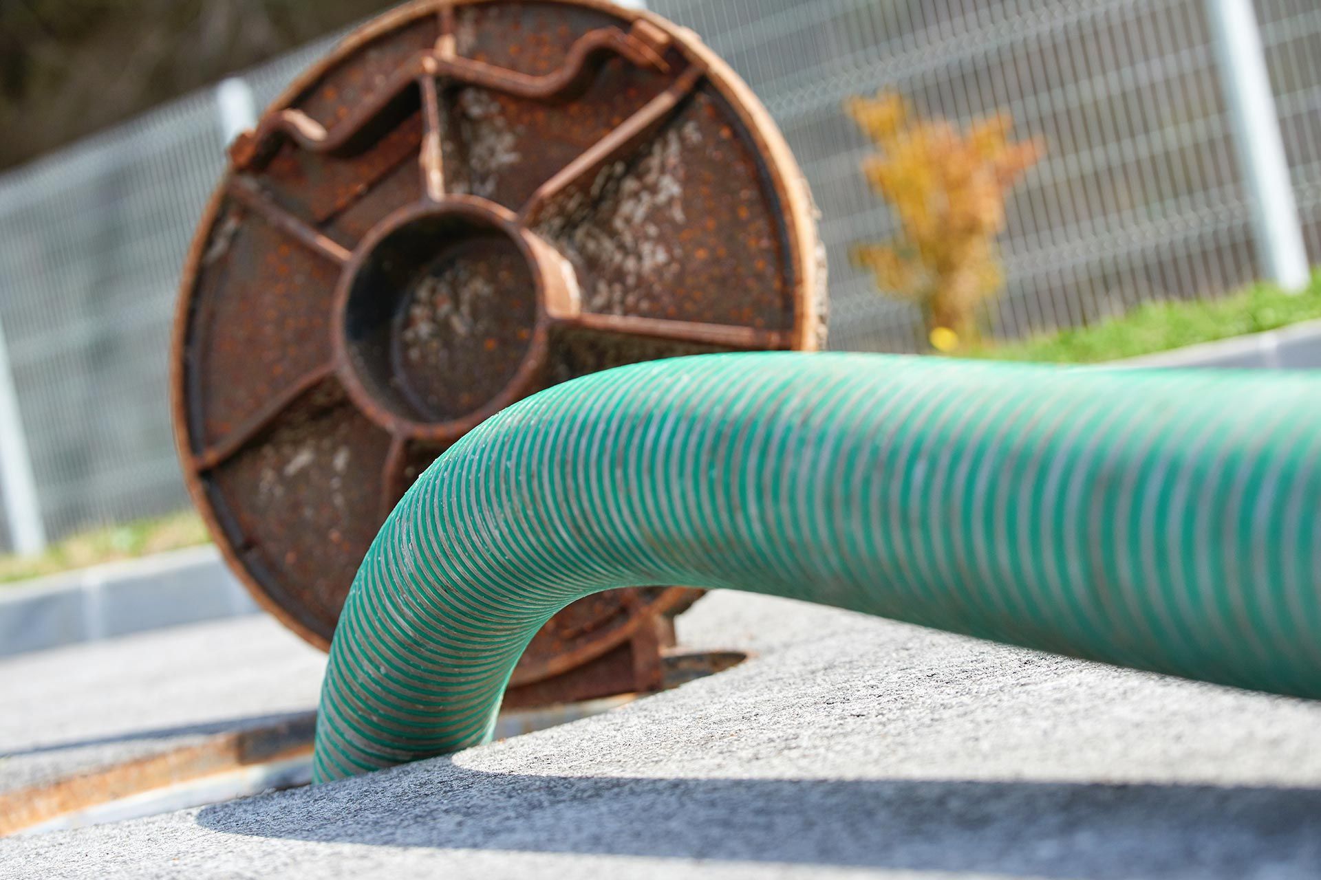 Green flexible hose inserted into an underground utility opening near a manhole cover.