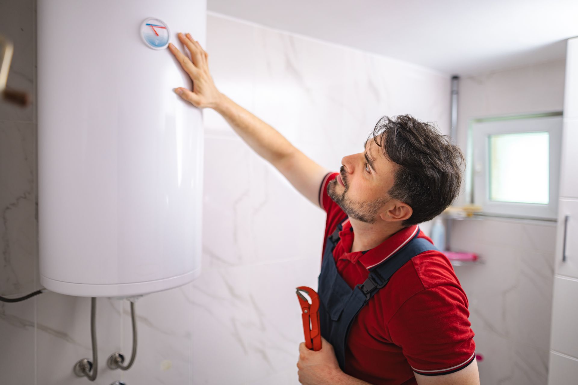Technician inspecting a wall mounted water heater while holding a wrench. Technician inspecting a wall mounted water heater while holding a wrench.