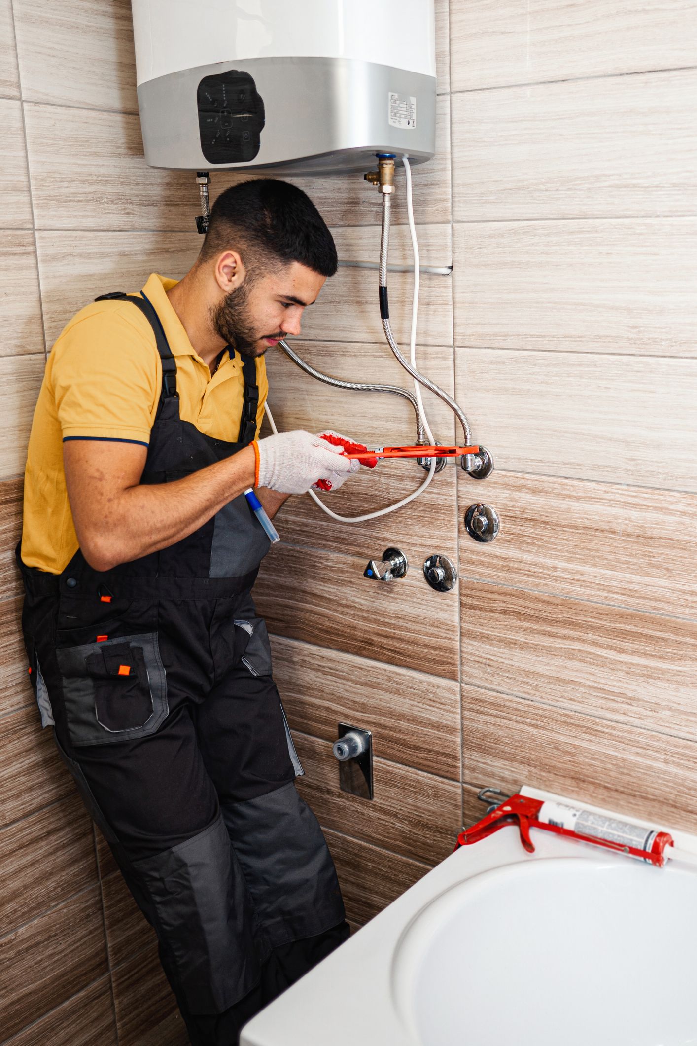 A technician in overalls tightens a hose on a heater, showcasing water heater replacement.